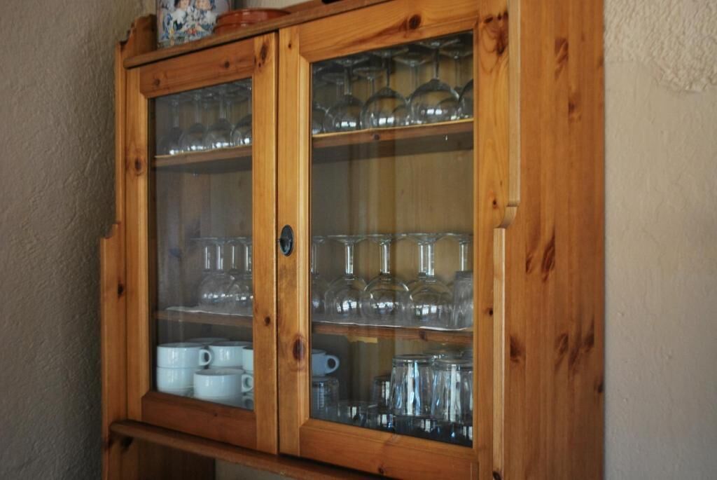 A wooden cabinet with glass doors containing various glassware and ceramic items.