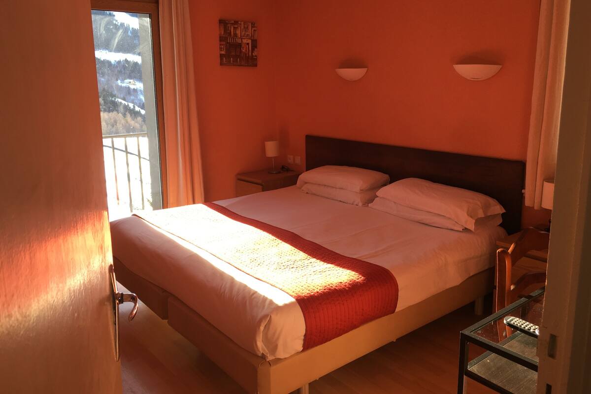 Une chambre d’hôtel avec un grand lit, une table de chevet, une lampe et une fenêtre avec des rideaux.