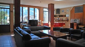 A spacious living area with a fireplace, leather sofas, and a large wooden table. - Hotel Roc de St Miquel (Soldeu)