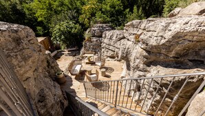 Eine Holzterrasse mit Gartenmöbeln, umgeben von felsigem Gelände und Bäumen.