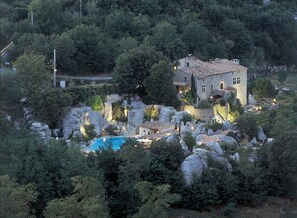 A stone building with a swimming pool surrounded by rocky terrain and dense greenery.