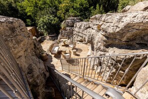 A wooden deck with outdoor furniture, surrounded by rocky terrain and trees. - Gîte Laumaga I 4 pers. I Spa privé I Domaine le C4 (Casteljau)