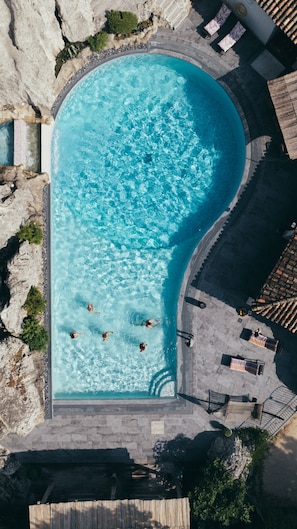 Vista aérea de uma piscina com borda curva, cercada por muros de pedra e um deck de madeira.