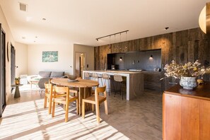 A modern kitchen with a central island, bar stools, and a dining area with a wooden table and chairs.