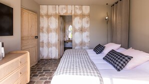 Ein Schlafzimmer mit einem großen Bett, einem Holzschrank, einem kleinen Schreibtisch und einem durch eine Holztür einsehbaren Badezimmer.