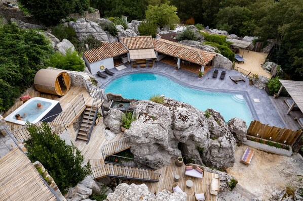 A pool area with a hot tub, wooden deck, and rock formations.