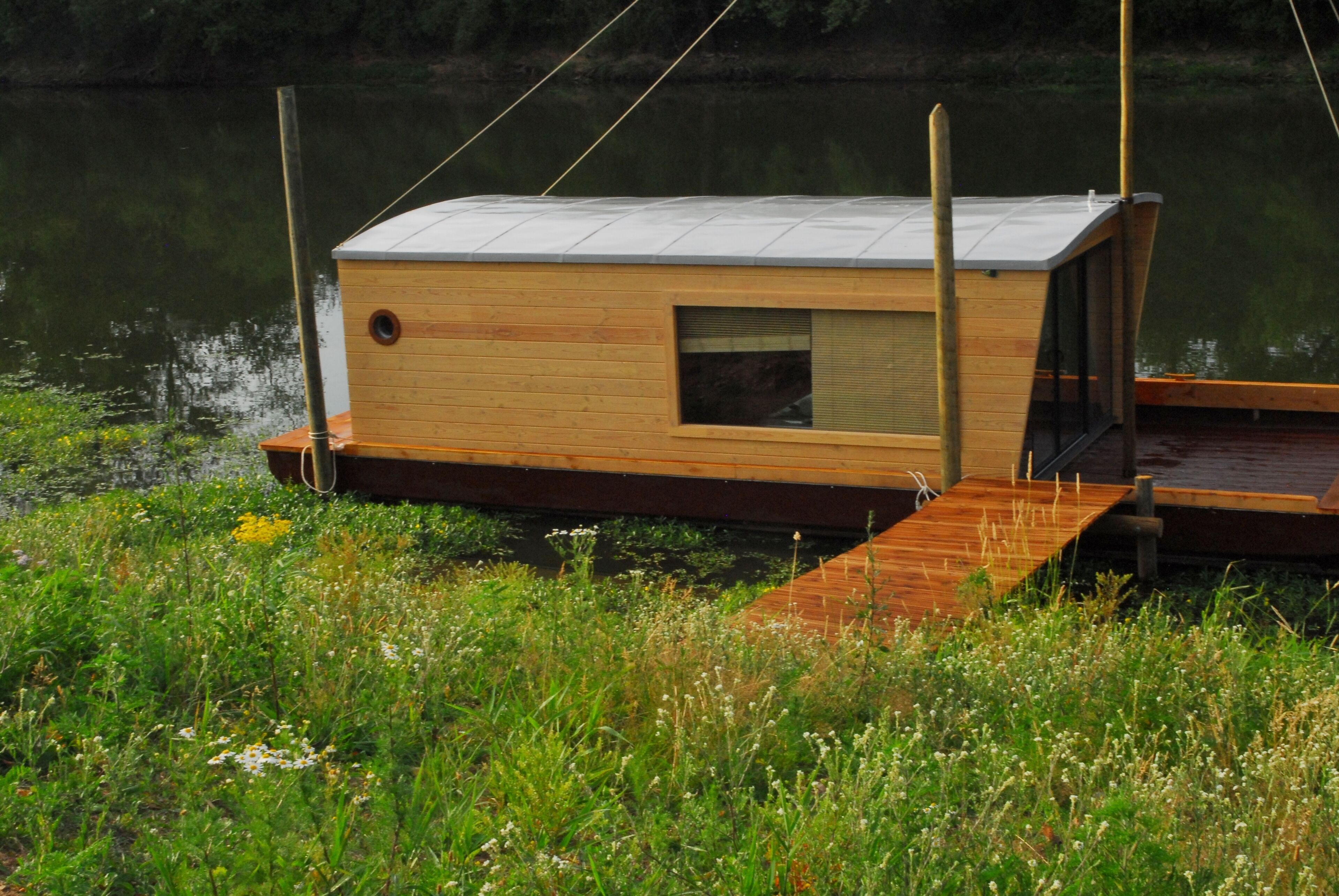 Une structure flottante en bois, dotée d’une fenêtre et d’une porte, et reliée à un quai.