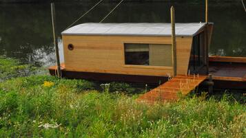 Une structure flottante en bois, dotée d’une fenêtre et d’une porte, et reliée à un quai.