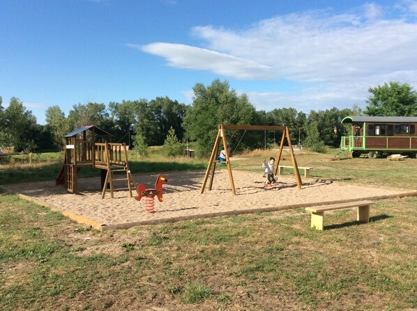 Un parque infantil con columpios, un tobogán y una pequeña estructura de madera.