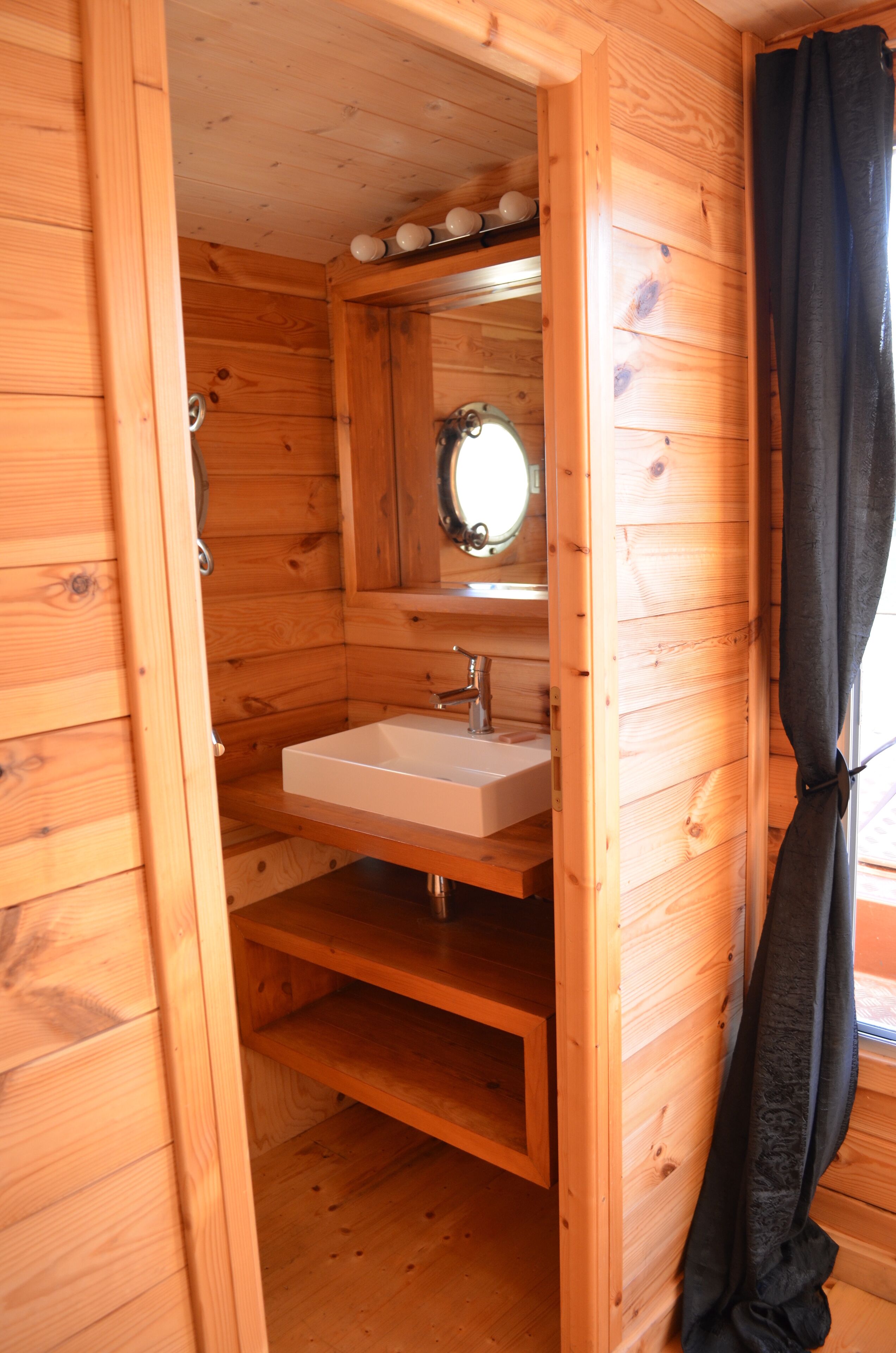 A wooden cabin bathroom with a white sink, a mirror, and a shelf above the sink.