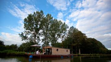 Une péniche avec une coque en bois, une petite terrasse et un espace couvert comprenant une table et des chaises.