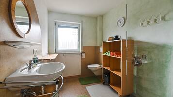 Une petite salle de bain comprenant un lavabo, un miroir, des toilettes et une étagère avec des serviettes.