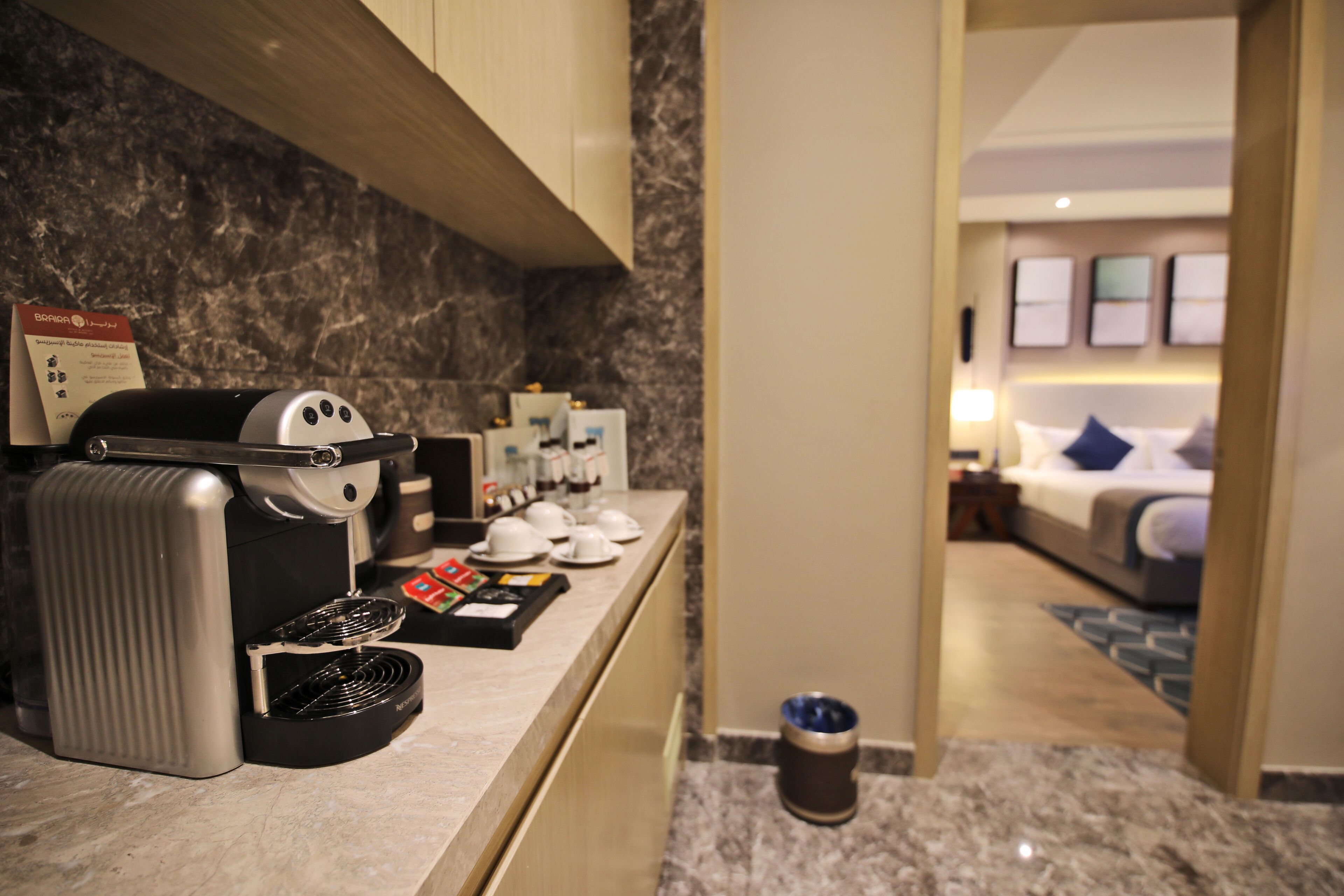 A hotel room with a marble countertop, a coffee machine, and a bed with a blue pillow.