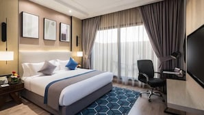 Habitación de hotel con una cama grande, un escritorio con silla, televisión y ventana con cortinas.