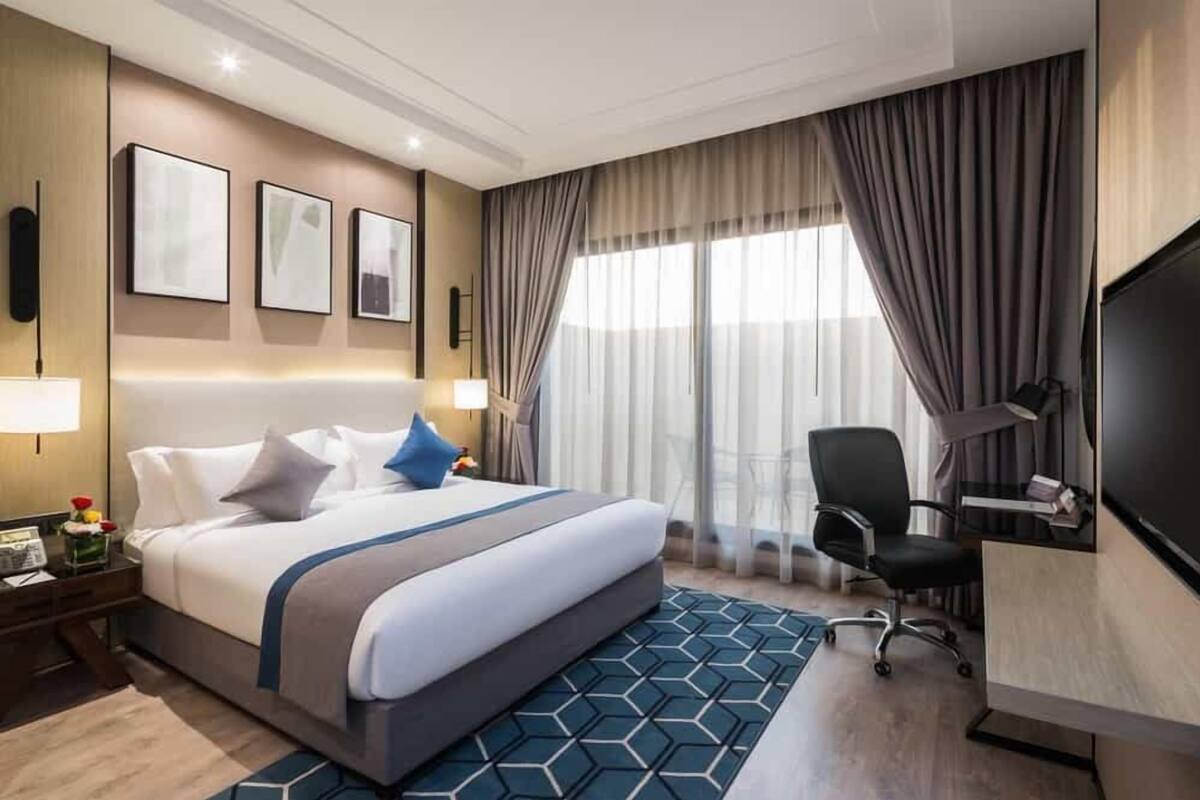 A hotel room with a large bed, a desk with a chair, a TV, and a window with curtains.
