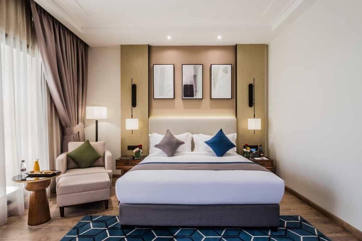 A hotel room with a large bed, a chair, a nightstand, and wall-mounted lamps.