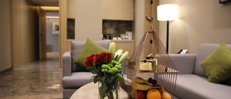 Un moderno vestíbulo de hotel con una mesa de centro de mármol, un jarrón con flores, una cesta de frutas y un sofá con cojines.