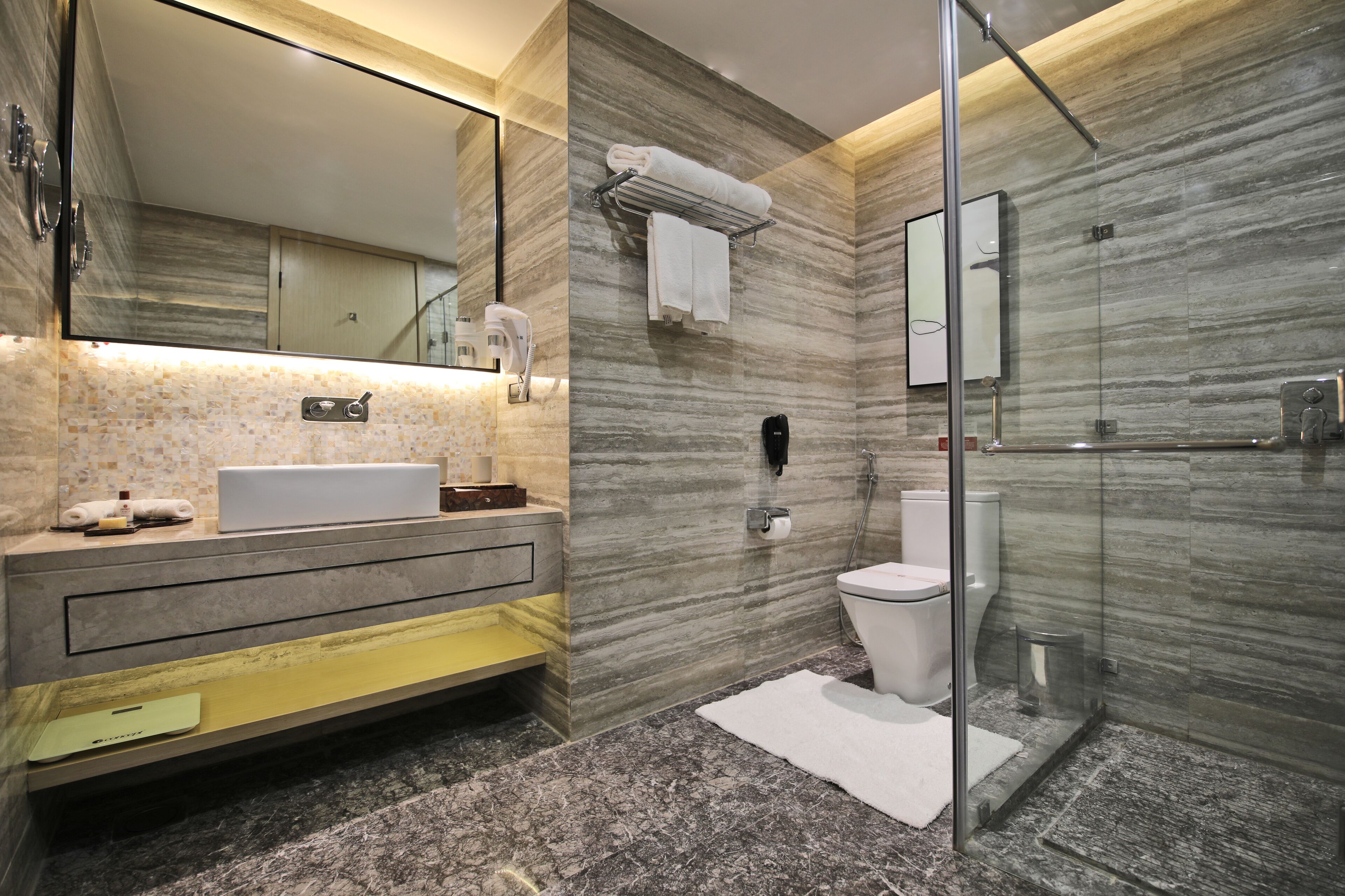 Un baño moderno con lavamanos de mármol, ducha con mampara de cristal y un espejo grande.