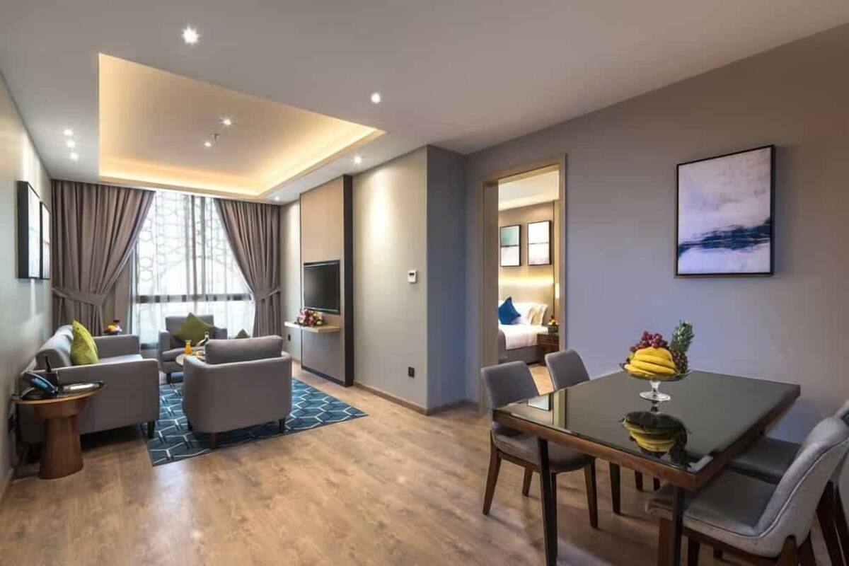 A modern hotel room with a living area, dining space, and a large window with curtains.
