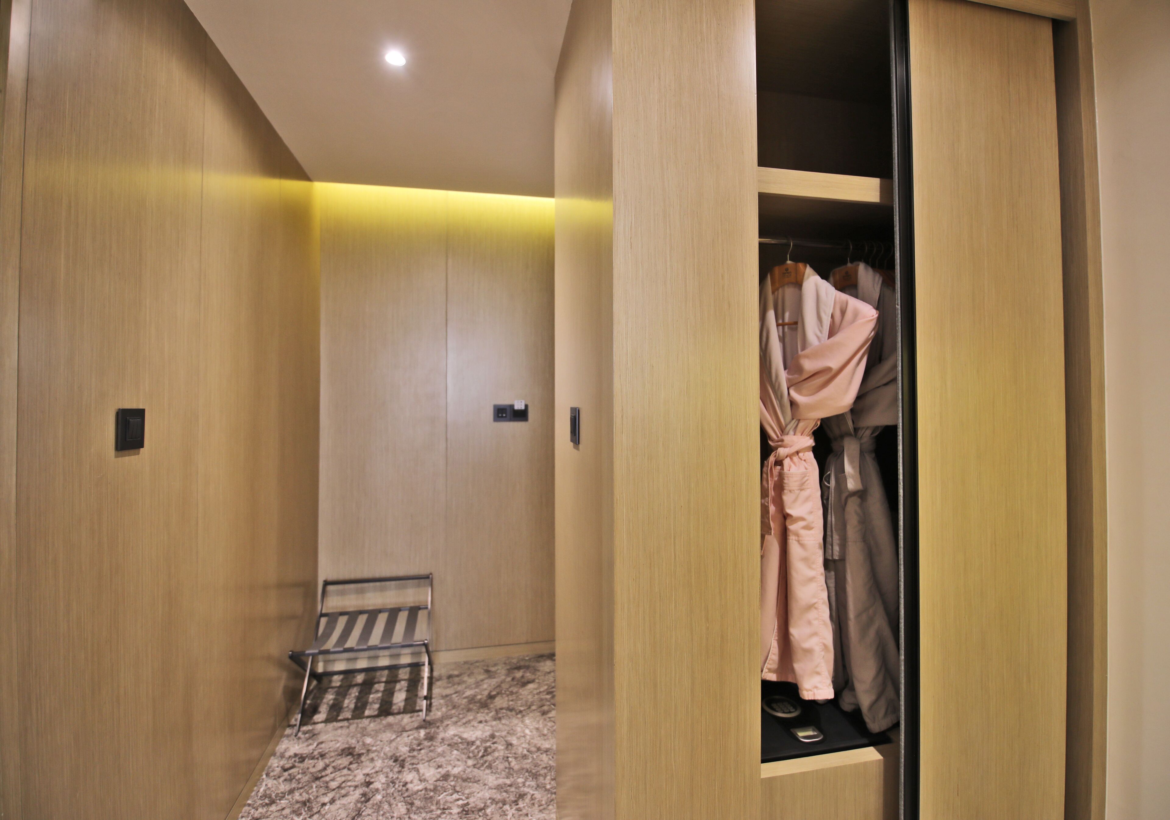 A modern hotel room with a wooden wardrobe, a bench, and a mirror.