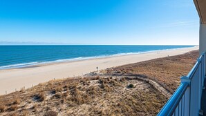A beach view from a balcony with a clear sky, sandy beach, and distant mountains. - Newly renovated 2 bedroom, 2 bath condo with beautiful views of the ocean! (Ocean City)