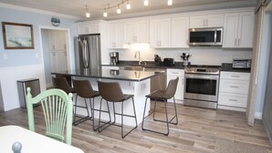 A modern kitchen with white cabinets, stainless steel appliances, and a central island with bar stools. - Newly renovated 2 bedroom, 2 bath condo with beautiful views of the ocean! (Ocean City)