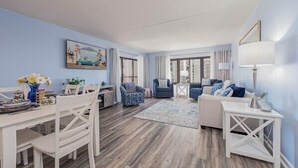 Una sala de estar moderna con comedor, que cuenta con un gran ventanal, un cuadro y una decoración azul y blanca.