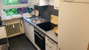 A compact kitchen with a window, a sink, a stove, and a refrigerator.