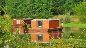 Two wooden floating houses on a calm lake, surrounded by lush greenery. - Toue cabanée spa (Chassenard)