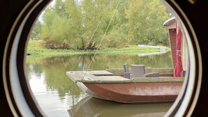 A boat docked at a calm lake with a red structure nearby, surrounded by lush greenery. - Toue cabanée spa (Chassenard)