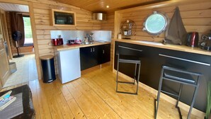 A compact kitchen with wooden walls, a microwave, a sink, a small fridge, and a window with a view. - Toue cabanée spa (Chassenard)