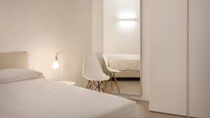 Un dormitorio minimalista con cama, una silla, una mesita de noche, una lámpara y un espejo grande.