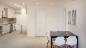 Una cocina moderna con armarios blancos, lavavajillas y una zona de comedor con mesa negra y sillas blancas.