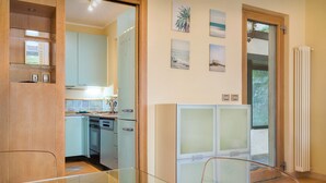 Een moderne keuken met lichtblauwe kastjes, een vaatwasser en een ingebouwde oven. Er hangen drie ingelijste foto's aan de muur, en op de voorgrond een glazen balustrade.