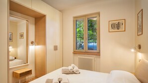 Een hotelkamer met een bed, een raam met uitzicht op groen, een houten nachtkastje en een spiegel.