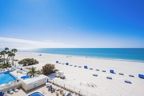 A beach resort with a swimming pool, sun loungers, and a view of the ocean.