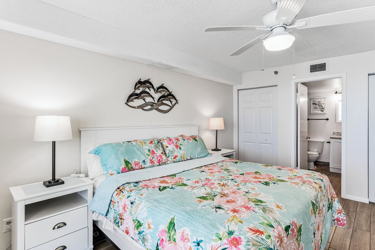 A bedroom with a bed, two bedside tables, a ceiling fan, and a door leading to a bathroom.