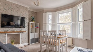 Ein gemütliches Wohnzimmer mit Kamin, Fernseher und Essbereich mit weißen Stühlen und einem Holztisch.