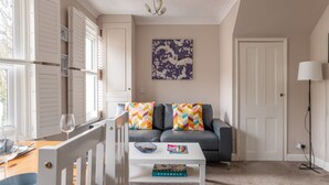 Ein Wohnzimmer mit grauem Sofa, bunten Zickzack-Kissen, einem weißen Couchtisch mit Büchern und einem Wandbild.