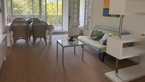 Una habitación con una mesa de comedor, sillas, un sofá, una mesa baja de vidrio y una estatua de Buda.