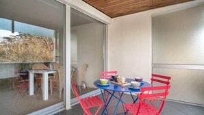 Un balcón con una mesa y sillas, una puerta corredera de vidrio y vistas a árboles.