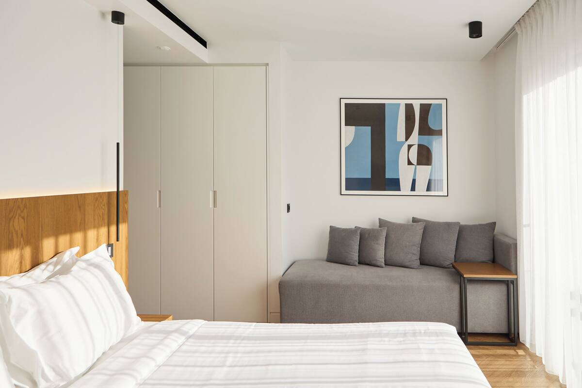 A modern hotel room with a bed, a sofa, a small table, and a painting on the wall.