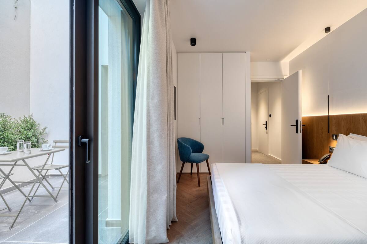 A modern hotel room with a bed, a chair, a desk, and a view of the outdoors.