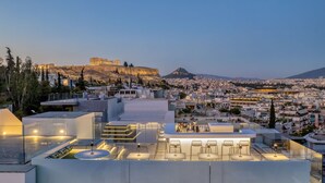 A rooftop terrace with modern furniture and a view of ancient ruins in the background. - Neoma  (Athens)