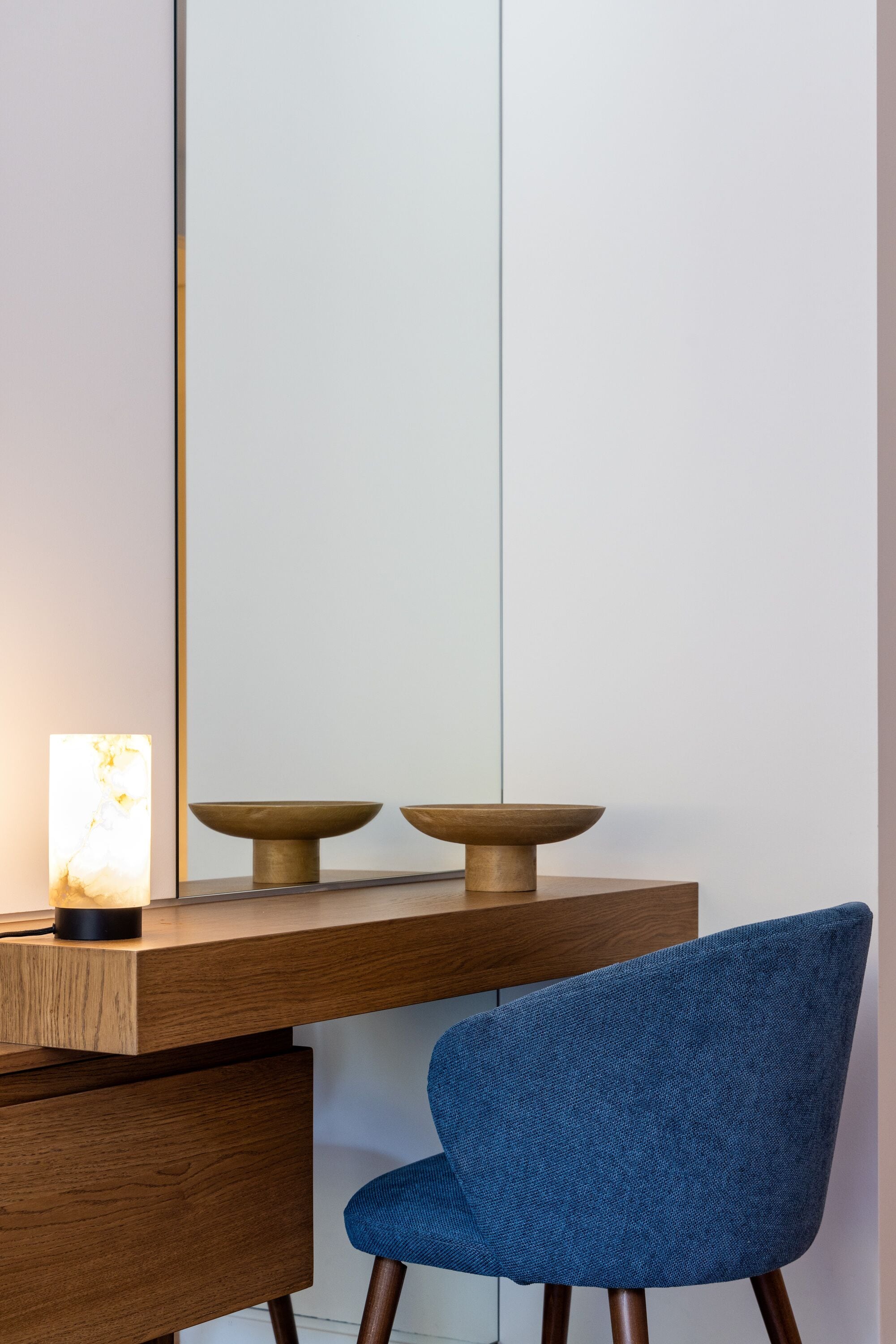 A modern desk with a wooden finish, two bowls on top, and a blue chair.