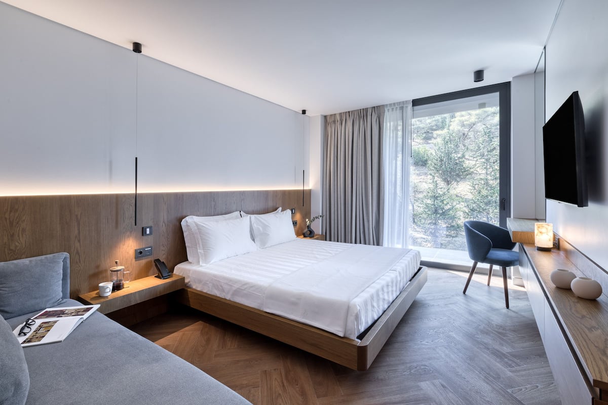 A modern hotel room with a large bed, a sofa, a desk, and a TV.