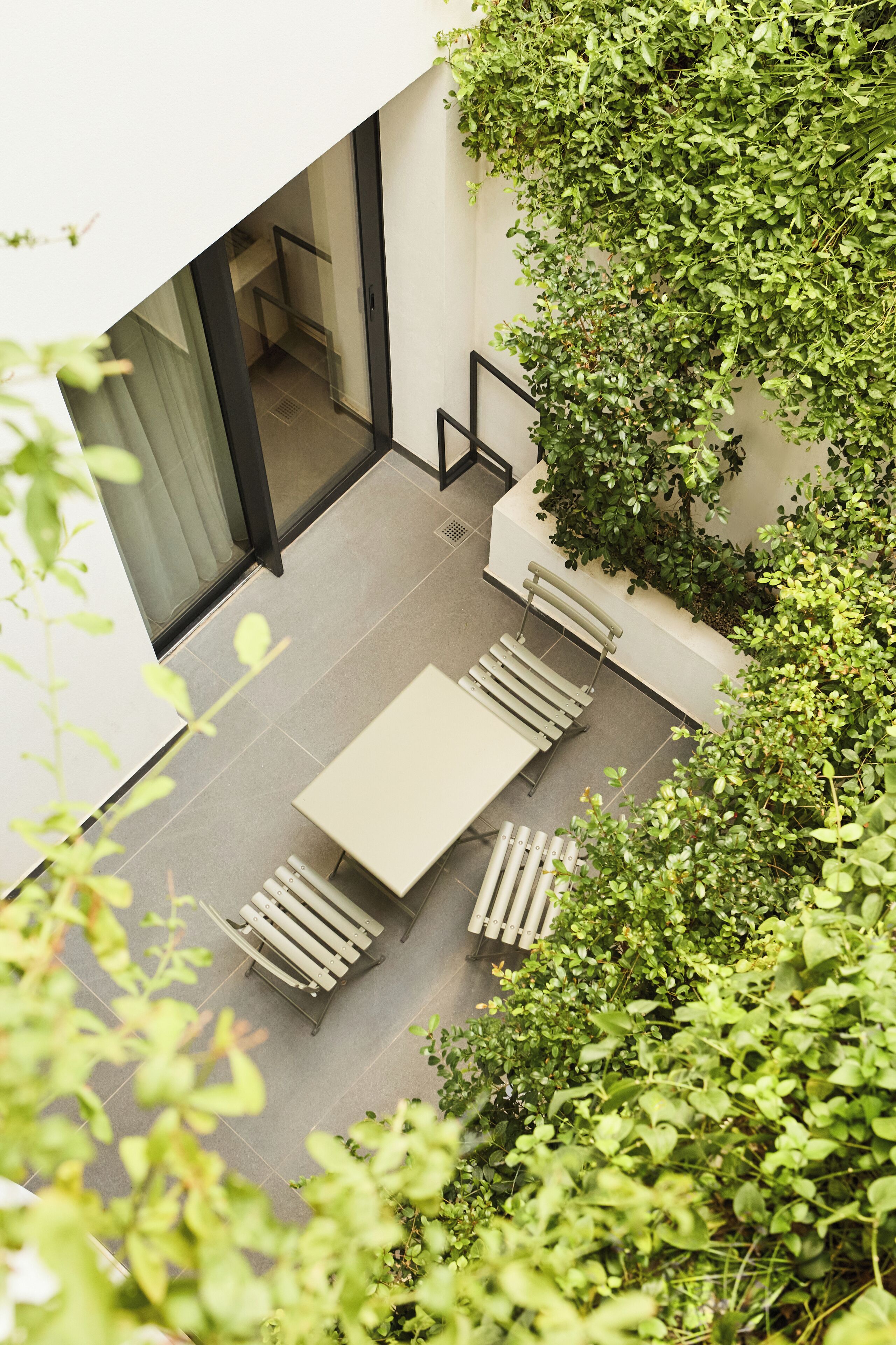 A modern outdoor patio with a table and chairs, surrounded by lush greenery.