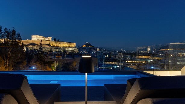 A rooftop terrace with a pool, seating area, and a view of the Acropolis at dusk. - Neoma  (Athens)