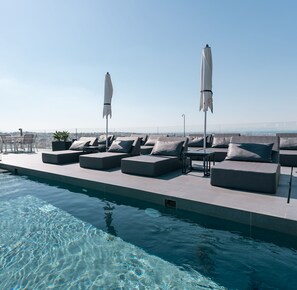 Un espace piscine sur le toit, avec des chaises longues et des parasols, offrant une vue dégagée sur le paysage urbain, et une piscine où règne la tranquillité.