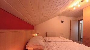 A bedroom with a bed, a red wall, a white ceiling, and a heart-shaped decoration on the wall. - Poludnig, cozy 5 P apartment (Presseggersee)